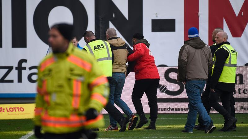 Ein Anhänger von Hansa Rostock wird von Sicherheitskräften vom Platz geführt.