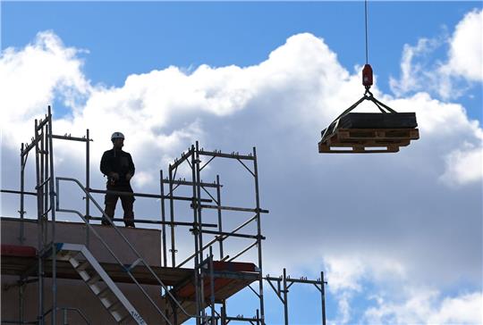 Ein Arbeiter dirigiert auf einer Baustelle einen Kran (Symbolbild). Foto: dpa
