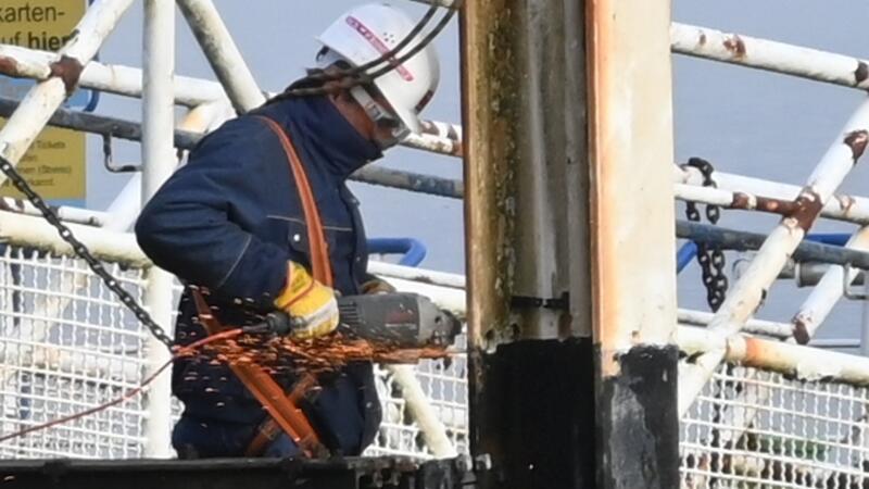 Ein Arbeiter flext am Lühe-Anleger den Stahlträger des Tors an der Landungsbrücke durch.