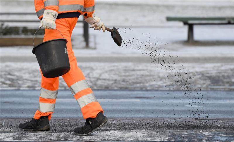 Ein Arbeiter in Schutzkleidung ist auf einem Gehweg mit Streuarbeiten beschäftigt. Foto: Ralf Hirschberger/dpa-Zentralbild/dpa
