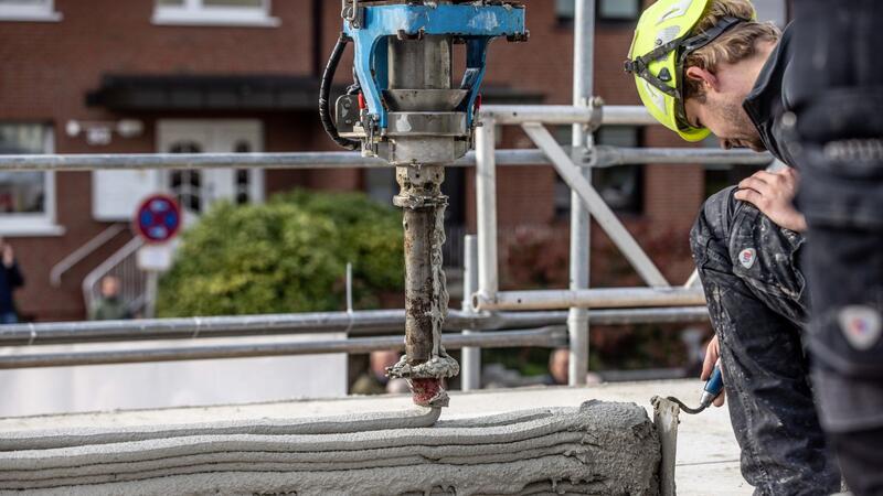 Ein Arbeiter inspiziert die Baustelle eines Mehrfamilienhauses aus dem 3D-Drucker.