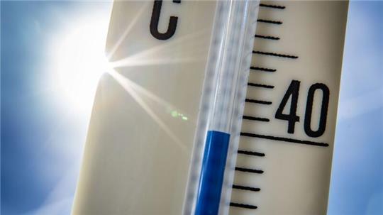 Ein Außenthermometer zeigt vor dem blauen Himmel und der Sonne eine Temperatur von nahezu 40 Grad Celsius an.