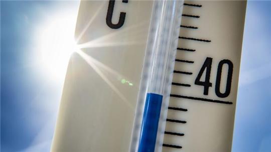 Ein Außenthermometer zeigt vor dem blauen Himmel und der Sonne eine Temperatur von nahezu 40 Grad Celsius an.