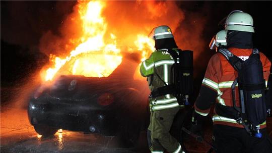 Ein Auto brennt, die Feuerwehr rückt unter Atemschutz vor.