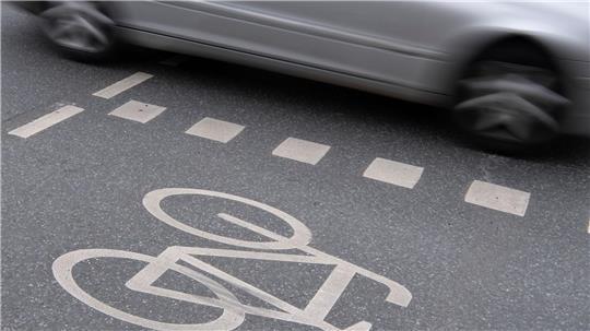 Ein Auto fährt an einer Kreuzung an einem Radweg vorbei. (Symboldbild)