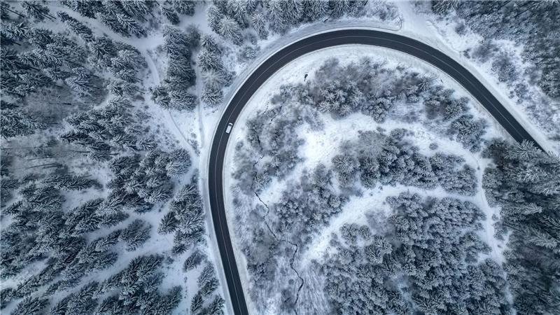 Ein Auto fährt auf einer Landstraße durch den winterlichen Wald im Vogtland.