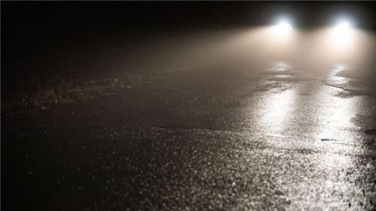 Ein Auto fährt durch Nebel auf einer Straße.