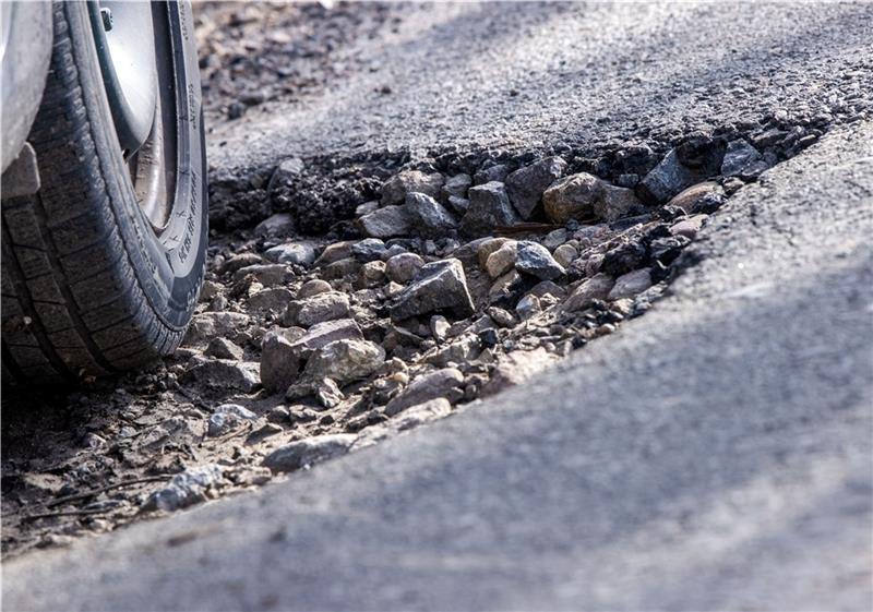 Ein Auto fährt durch ein Schlagloch auf einer Alleestraße. Foto: Jens Büttner/dpa-Zentralbild/dpa +++ dpa-Bildfunk +++