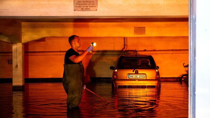 Ein Auto steht im Stadtteil Billstedt in einer durch Starkregen überfluteten Tiefgarage und wird vom Licht einer Warnblinkanlage angeleuchtet.