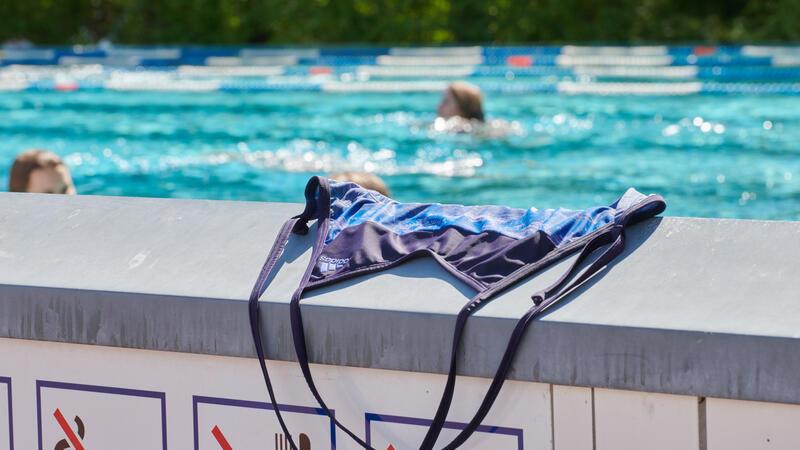 Oben ohne am Elbstrand oder nackt im Supermarkt? Das ist erlaubt Ein Badeanzug liegt auf einer Mauer im Prinzenbad, dahinter schwimmen Menschen im Becken ihre Bahnen.