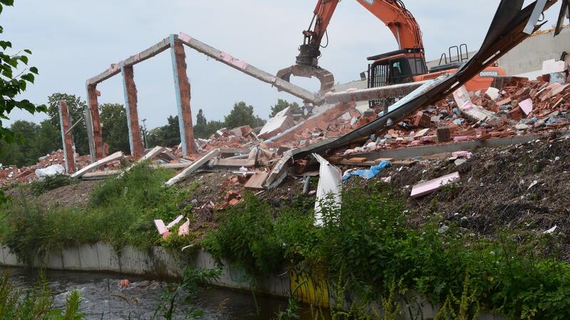Ein Bagger reißt eine Wand des früheren Lidl-Marktes in Altkloster ab. Bei den Abbrucharbeiten fallen einzelne Steine in den Wasserlauf der Fischumgehung.