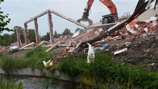 Ein Bagger reißt eine Wand des früheren Lidl-Marktes in Altkloster ab. Bei den Abbrucharbeiten fallen einzelne Steine in den Wasserlauf der Fischumgehung.