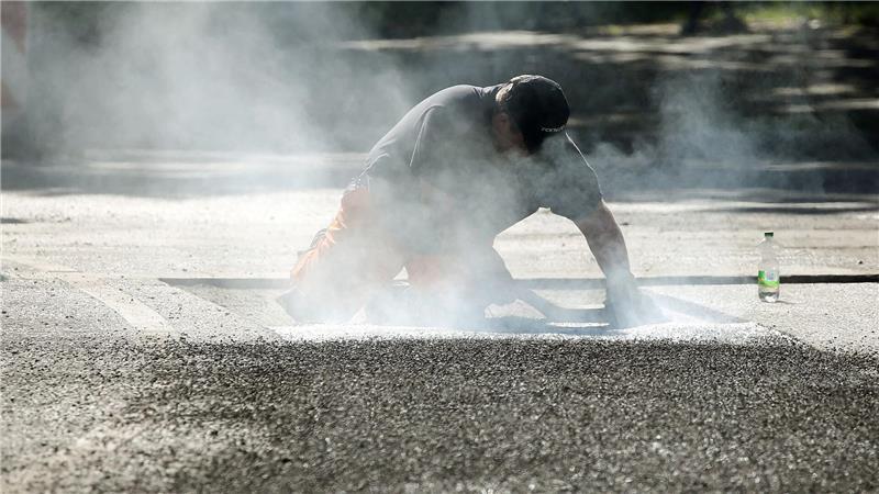 Ein Bauarbeiter repariert eine Straße in Berlin mit Bitumen, einem Bindemittel für Asphalt. (Symbolbild)