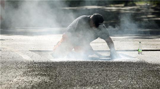 Ein Bauarbeiter repariert eine Straße in Berlin mit Bitumen, einem Bindemittel für Asphalt. (Symbolbild)