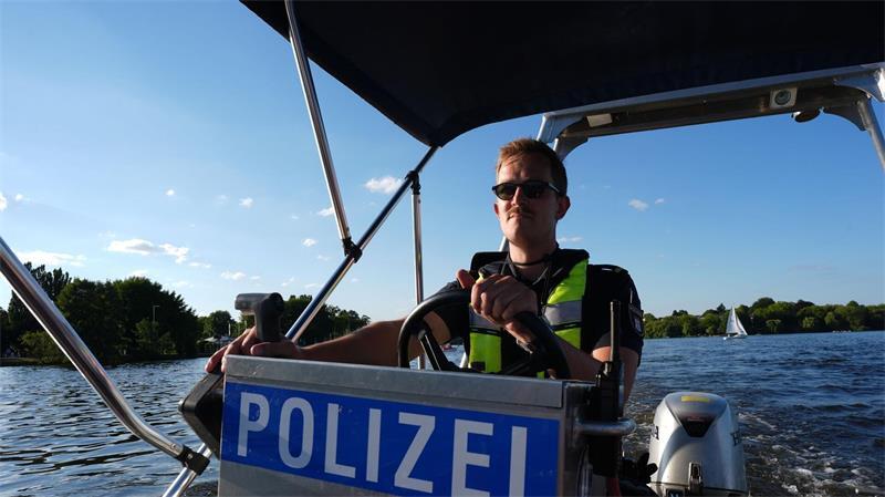 Ein Beamter steuert ein Polizeiboot mit Benzinmotor über die Alster.