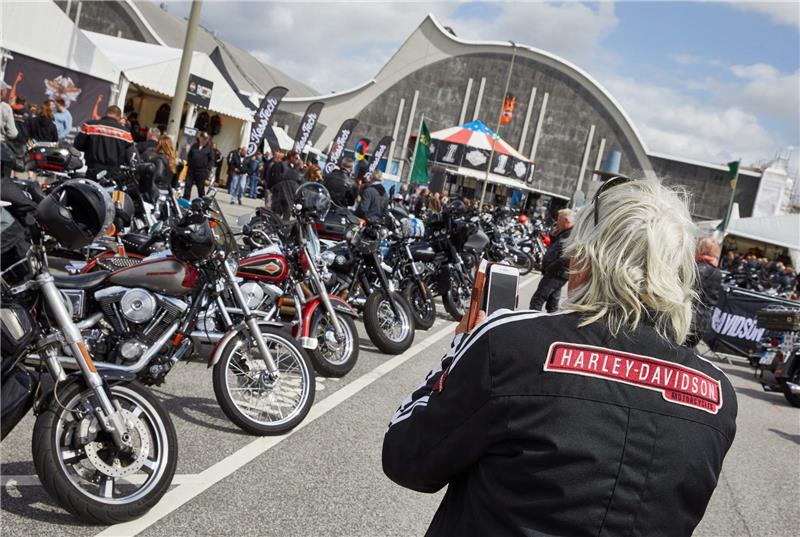Ein Besucher mit dem Schriftzug "Harley Davidson" auf seinem Rücken fotografiert auf dem Festivalgelände der Harley Days Motorräder.  Foto Georg Wendt/dpa