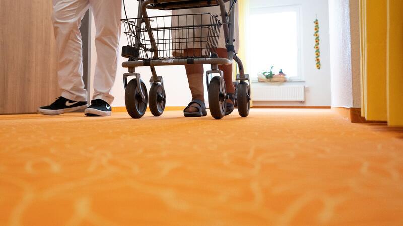 Erhebung: Pflegeheimbewohner müssen mehr zahlen Ein Betreuer geht in einem Pflegeheim mit einer Bewohnerin über den Flur.