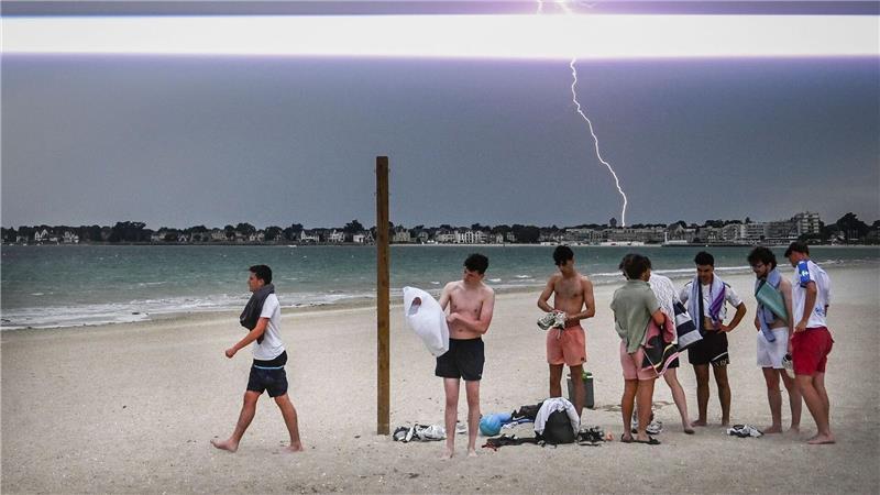 Ein Blitz erhellt den Himmel, während Menschen den Strand während eines Gewitters über der Stadt La Baule im Westen Frankreichs verlassen.