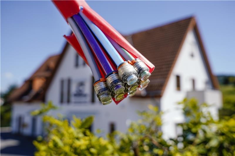 Ein Bündel mit Umhüllungen für Glasfaserkabel hängt an einem Schild und vor einem Wohnhaus. Foto: Uwe Anspach/dpa (Symbolbild)