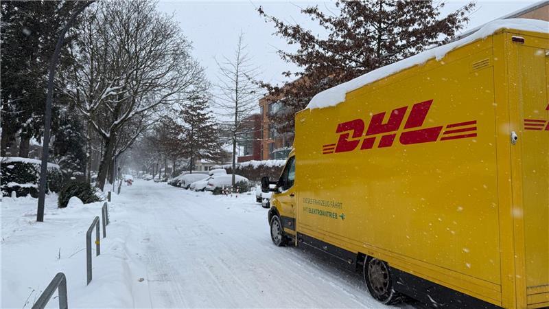 Ein DHL-Lieferfahrzeug ist auf einer verschneiten Straße im Hamburger Stadtteil Lokstedt unterwegs.