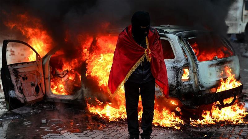 Ein Demonstrant, der sich in eine albanische Flagge gehüllt hat, steht während einer regierungskritischen Demonstration in Tirana vor dem Büro des Ministerpräsidenten vor einem brennenden Auto.