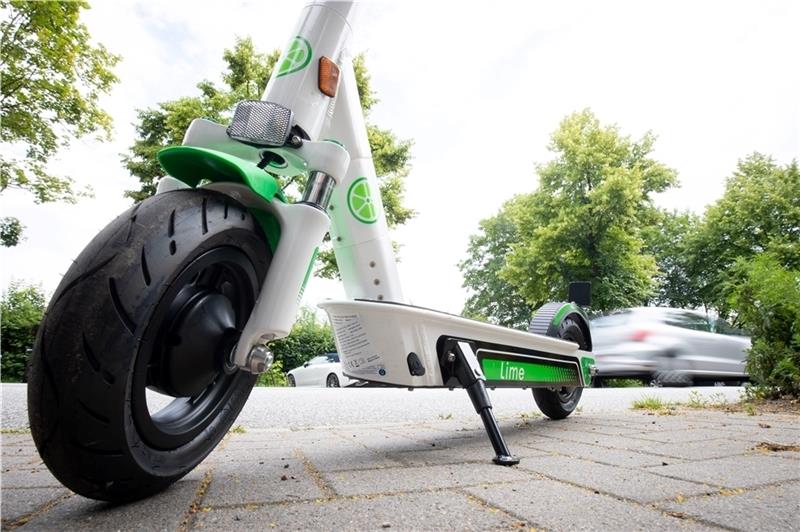 Ein E-Tretroller zum Mieten steht auf einem Parkplatz am Straßenrand. Die Standorte der Roller des amerikanischen Unternehmens Lime werden auf einer Smartphone-App angezeigt. Foto:Charisius/dpa