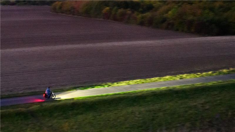 Ein Fahrradfahrer fährt am frühen Morgen mit Licht über einen Feldweg bei Hannover.