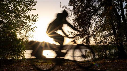 Ein Fahrradfahrer fährt bei Sonnenaufgang am Ufer des Templiner Sees entlang.