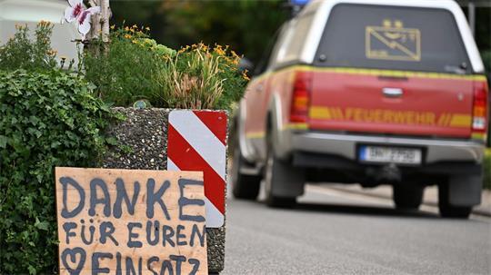 Ein Fahrzeug der Feuerwehr fährt an einem Schild mit der Aufschrift „Danke für Euren Einsatz“ beim Waldbrand im Hürtgenwald vorbei. 