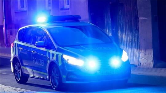 Ein Fahrzeug der Polizei fährt mit Blaulicht am Abend durch eine enge Straße.