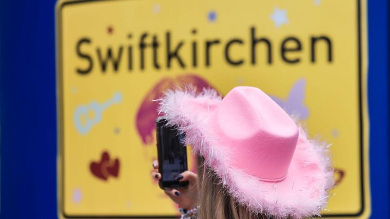Ein Fan fotografiert vor dem Konzert der Sängerin Taylor Swift in Gelsenkirchen ein „Swiftkirchen“-Schild. Während des Konzerts am Abend zog der Datenverbrauch in den Handynetzen in der Veltins Arena kräftig an.