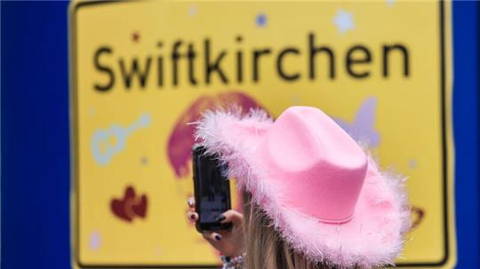 Ein Fan fotografiert vor dem Konzert der Sängerin Taylor Swift in Gelsenkirchen ein „Swiftkirchen“-Schild. Während des Konzerts am Abend zog der Datenverbrauch in den Handynetzen in der Veltins Arena kräftig an.