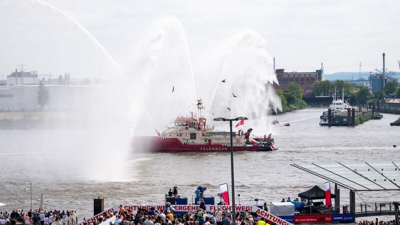 Hamburger Hafengeburtstag startet mit großer Einlaufparade Ein Feuerlöschboot fährt an den Landungsbrücken mit Wasserfontänen entlang.