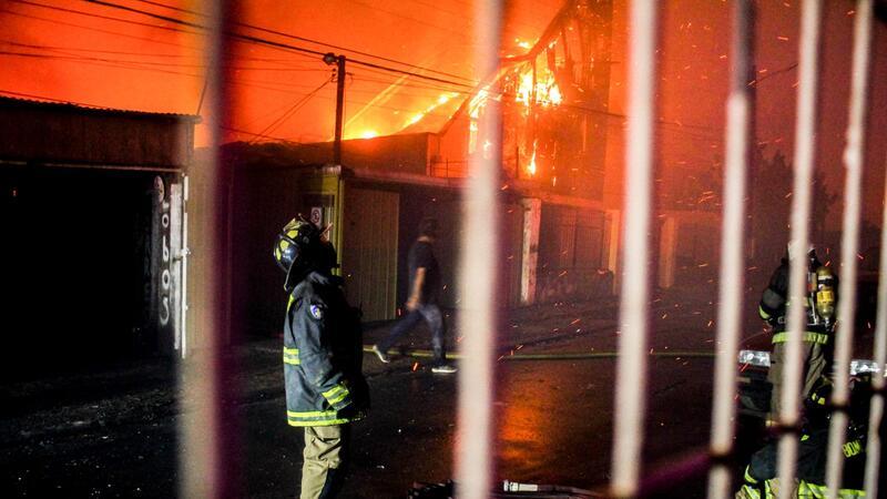 Ein Feuerwehrmann blickt nach oben, als die Flammen eines Waldbrandes auf Gebäude übergreifen.