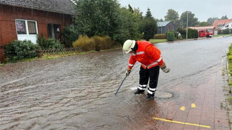Ein Feuerwehrmann kontrolliert bei Starkregen eine überflutete Straße in Hemmoor.