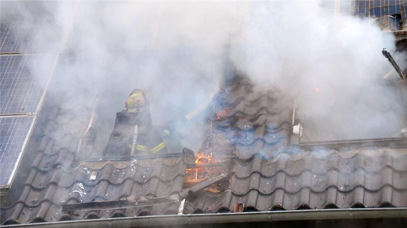 Ein Feuerwehrmann löscht aus einem Dachfenster heraus neben der Photovoltaikanlage.
