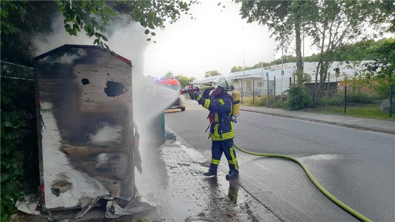 Ein Feuerwehrmann löscht die brennenden Altkleidercontainer.