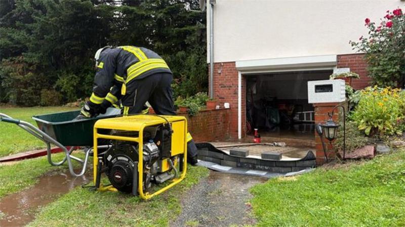 Ein Feuerwehrmann pumpt nach dem Starkregen in Hemmoor Wasser aus einem überfluteten Bereich an einem Wohnhaus.