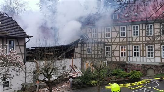 Ein Feuerwehrmann steht bei Löscharbeiten in der Nähe von den Klinik Gebäuden.