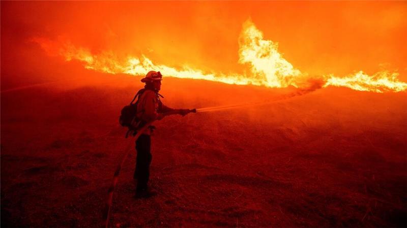 Ein Feuerwehrmann versprüht Wasser, während er die vom Hughes-Feuer in Kalifornien verursachten Flammen an einem Straßenrand überwacht.