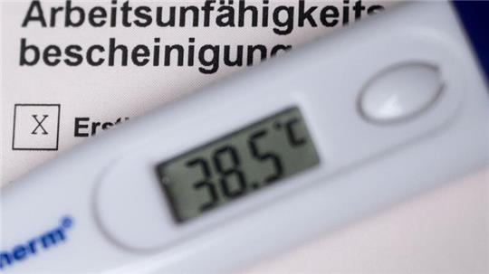Ein Fieberthermometer liegt auf einer Arbeitsunfähigkeitsbescheinigung.