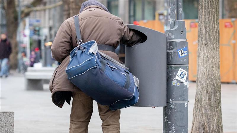 Ein Flaschensammler greift in eine Mülltonne 