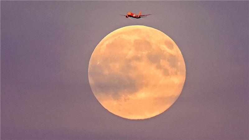 Ein Flugzeug fliegt vor dem sogenannten Supermond am frühen Abend über Leipzig.