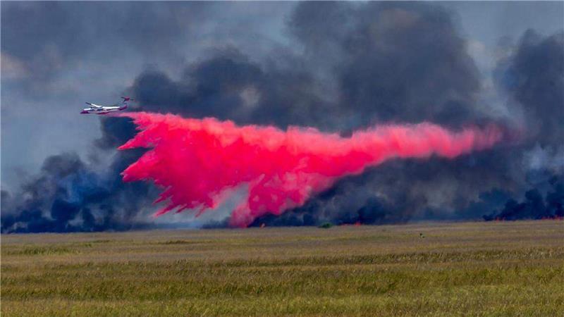 Ein Flugzeug wirft Feuerschutzmittel auf ein großes Waldfeuer.