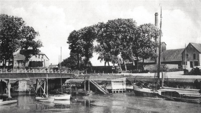 Ein Frachtsegler liegt an der Hafenkante. Im Hintergrund ist die Mühle mit ihrem markanten Schornstein zu sehen, die es einst im Großensieler Hafen gab und die maßgeblich zum Aufschwung beitrug.