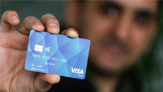 Ein Geflüchteter hält eine Debitcard in der Hand.