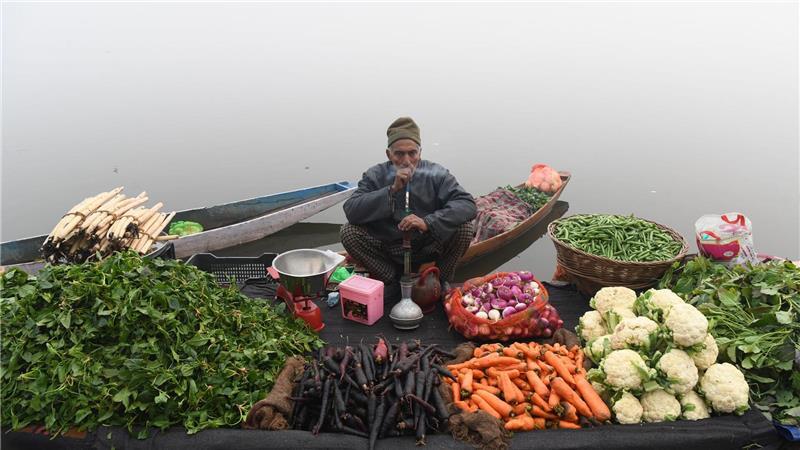 Ein Gemüsehändler raucht eine Wasserpfeife, während er an einem nebligen Tag am Ufer eines Sees im indischen Srinagar auf Kunden wartet.