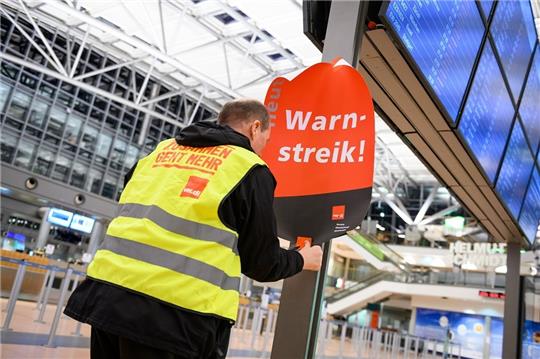 Ein Gewerkschaftsvertreter klebt ein Plakat mit der Aufschrift "Warnstreik!" und einen Flyer an die Anzeigetafel im leeren Terminal 2. Foto: Jonas Walzberg/dpa