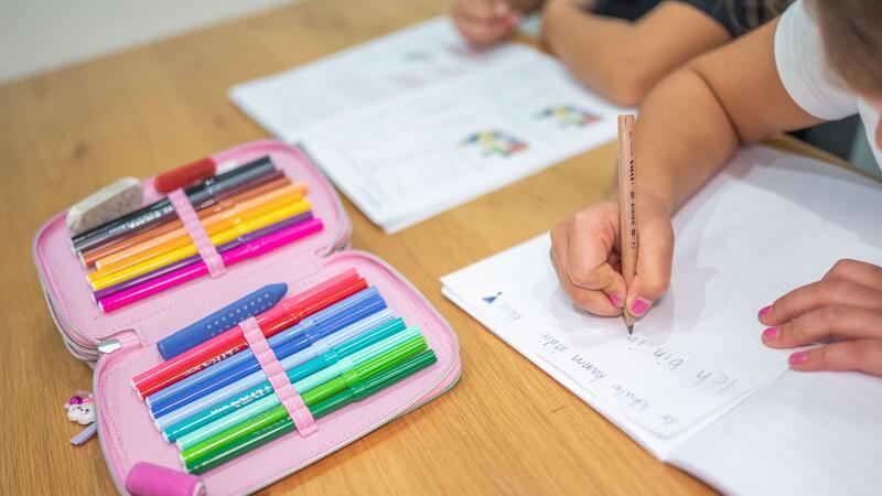 Ein Grundschüler und eine Grundschülerin sitzen in einem Wohnzimmer am Tisch und erledigen Schulaufgaben.