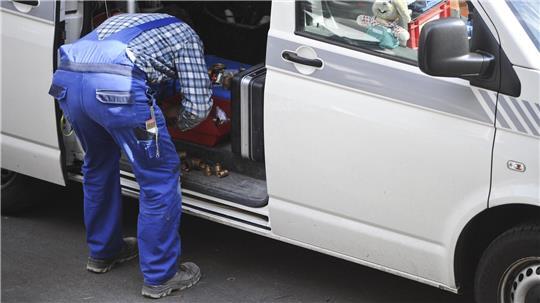 Ein Handwerker steht gebückt an seinem Auto (Symbolbild).
